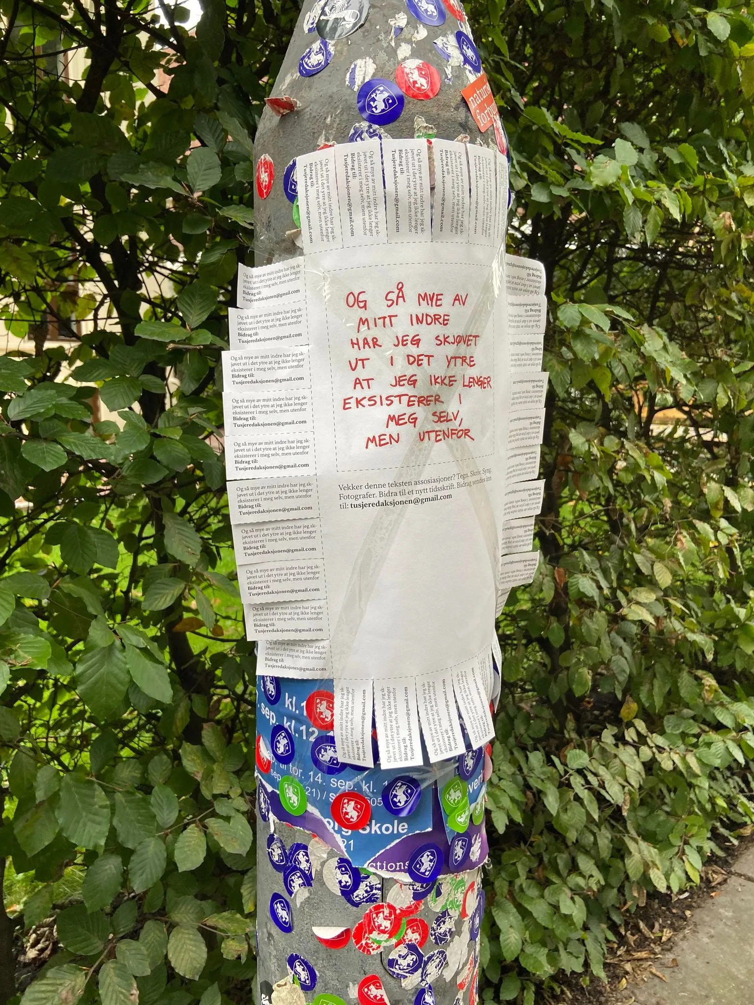 Lamppost covered in stickers with a Tekst1 call for contributions and tear-off email tabs