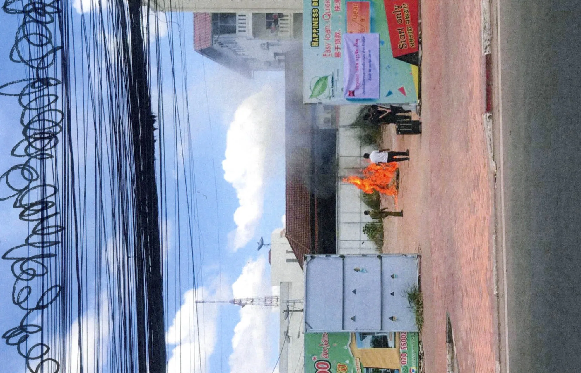 Rotated book spread photo of a street fire and power lines under blue sky, with scribbled loops