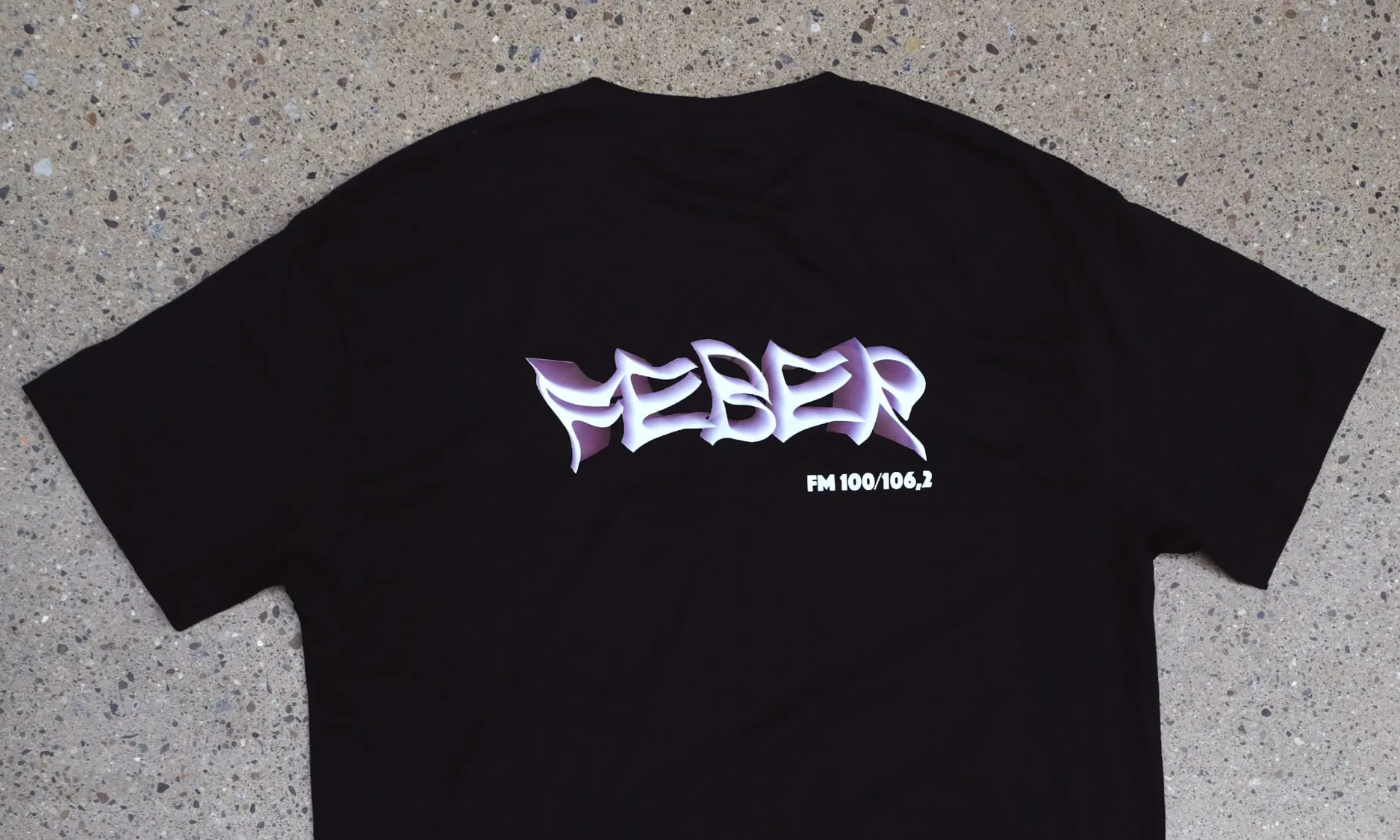 Black t-shirt with the FEBER FM 100/106,2 logo in purple 3D lettering on concrete