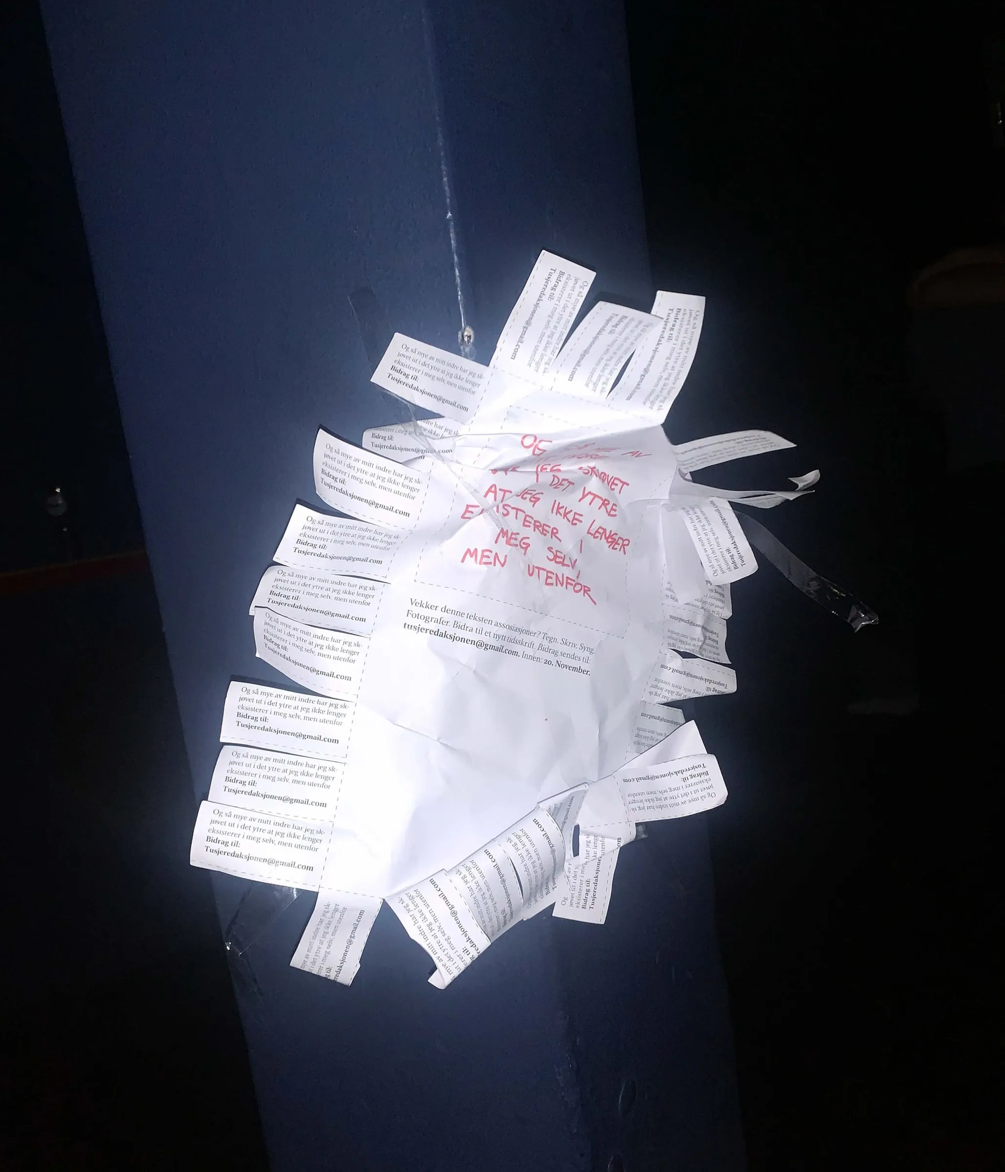 Crumpled Tekst1 flyer with tear-off strips and red handwritten text, taped to a blue pole at night