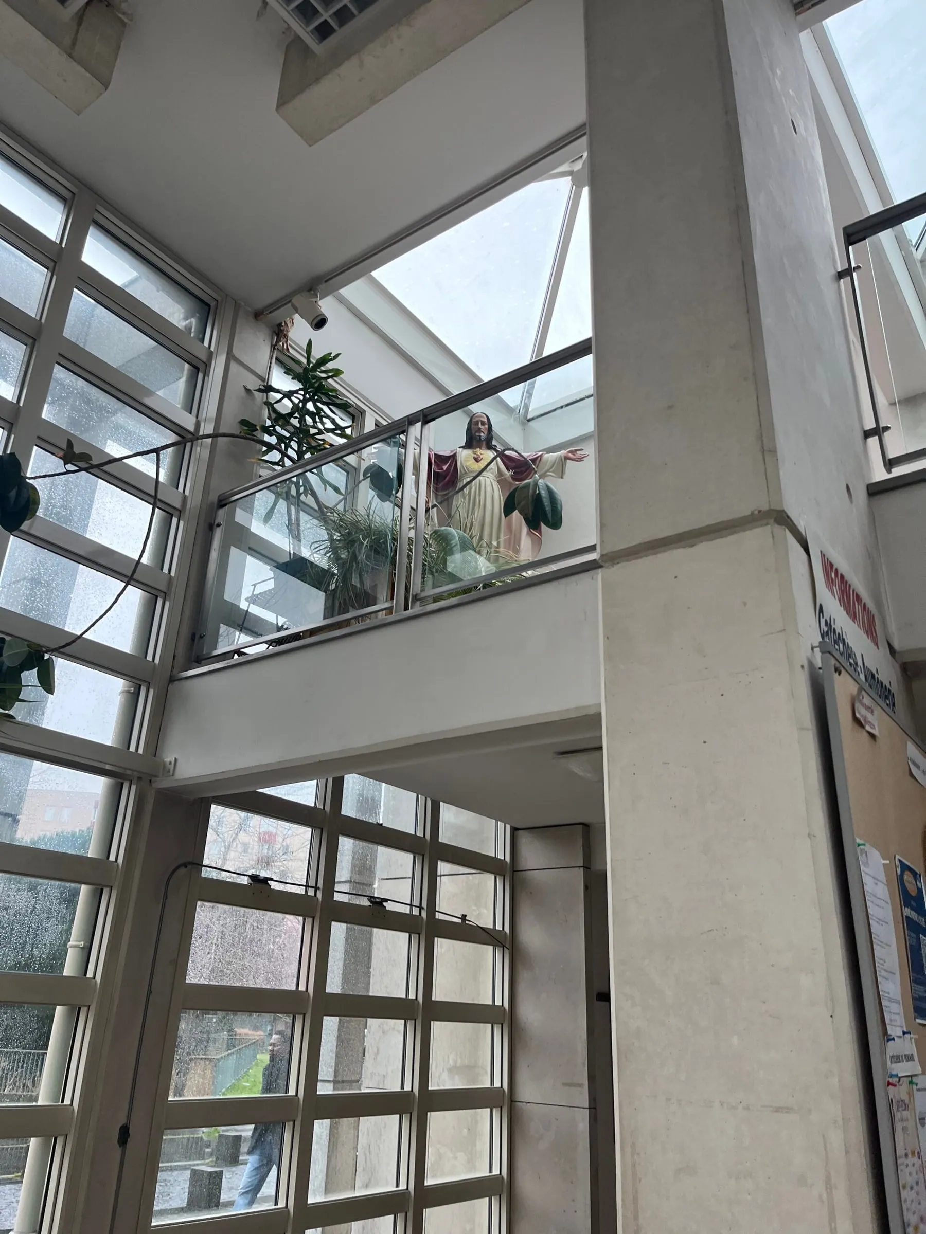Church interior with a Sacred Heart statue on a balcony among plants and big windows