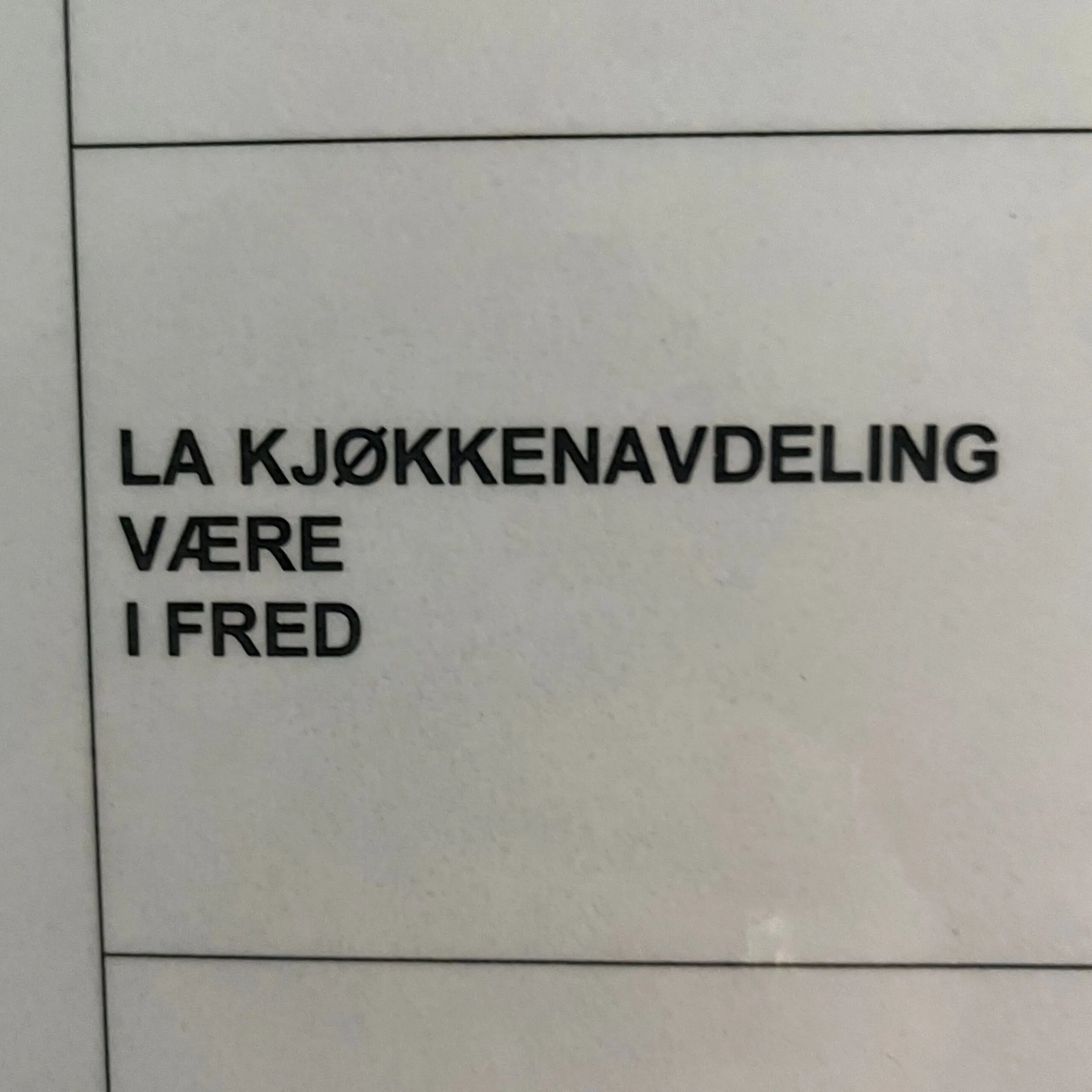 Black text on white sign reading LA KJØKKENAVDELING VÆRE I FRED